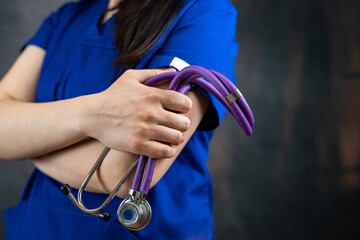 beautiful female doctor or medical student  in blue uiform with stethoscope against dark background