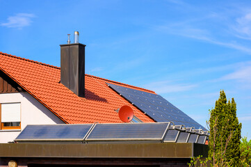 Solarthermieanlage auf Garagendach vor rotem Hausdach mit Photovoltaikanlage  - obrazy, fototapety, plakaty