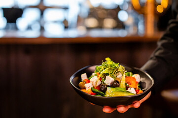 Server presenting a vibrant, fresh salad in a black bowl against a blurred restaurant background