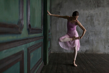 Slender ballerina in a pink suit inspects her pointe shoes before warming up