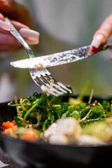 Person preparing a vibrant, fresh salad, mixing ingredients with a fork and knife. A moment of healthy meal preparation captured