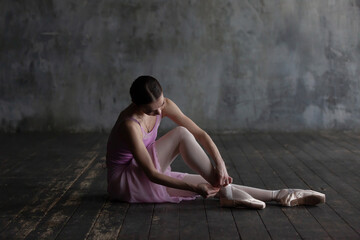 Graceful ballerina sits on a floor and puts on pointe shoes