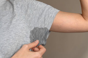 Close-up of a young woman shows a wet armpit on a gray T-shirt. Concept of health, sports