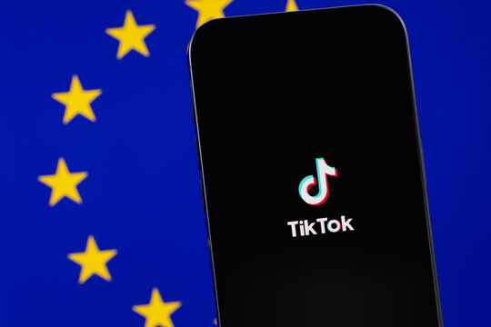 TikTok mobile icon app on screen smartphone iPhone, flag of Europe background. TikTok is app to create and share videos. Moscow, Russia - December 21, 2023