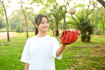 Smiling Asian girl wearing leather glove throwing baseball up into the air