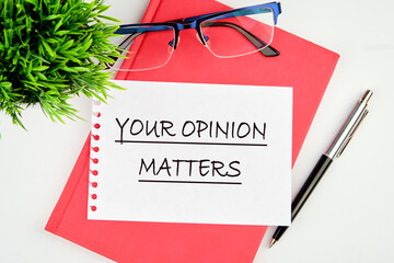 YOUR OPINION MATTERS phrase written on a piece of paper on a red notebook on a white background
