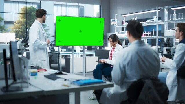 Head of Laboratory Showing Presentation on a TV Screen with Green Chroma Key Template. PhD Professor Teaching a Group of Science Students the Basics of Research in Biological Engineering