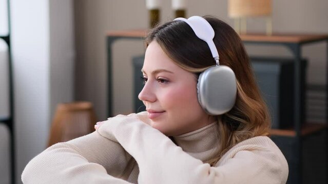 Portrait of a friendly Caucasian young woman enjoying music in headphones at home. Relaxation during weekend or holiday. Resting on sofa.