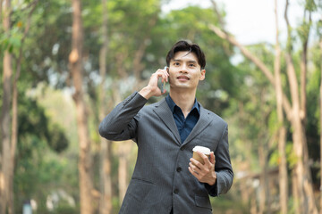 Handsome businessman holding paper cup of coffee and talking on mobile phone at outdoor