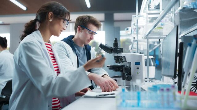 Molecular Biology Students Conducting Research in a Lab, Looking at DNA Sample Under a Microscope in an Applied Science Course in College. Young Female and Male Bioengineers Studying Science