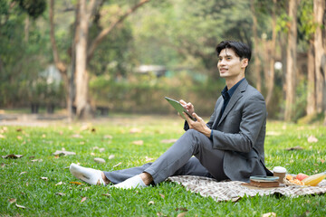 Portrait of handsome businessman sitting grass holding digital tablet and looking away