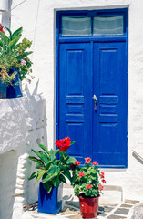Blau gestrichene Doppeltür eines weiß getynchten Wohnhauses oder einer Pension mit Blumenkübeln als Verzierung auf der grichischen Insel San Turin im Nachmittagslicht der Sonne - 788158774
