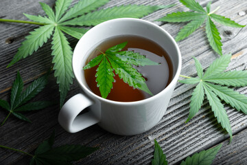 Cannabis tea with green marijuana leaves in white cup on wooden table. Medical herbal tea with cannabis close up
