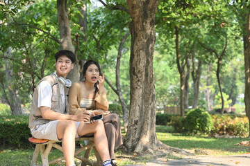 Happy young couple sitting together on bench in public park during summer day
