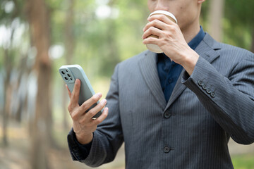 Cropped shot of businessman in formal suit drinking coffee and using mobile phone outdoor