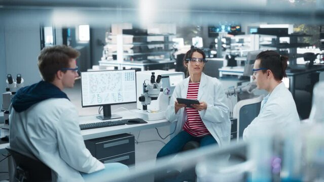 Female Medical Supervisor Having a Conversation with Two Young Scientist About a Gene Editing Research Project, Technology and Experiments. Smart Diverse Team Working in a Laboratory
