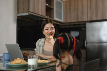 Happy asian mother working remotely at home and taking care of little daughter at kitchen table