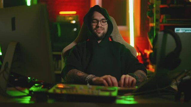 Hacker writing code cracking computer. Man programmer in hoodie cracks system, using computer in dark room. Hacker attack, technology, virus infected software, dark web, technology job concept.