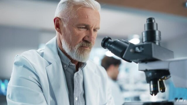 Medical Research and Development Laboratory: Middle Aged Head Scientist Working on Research Project, Looking at a Biological Sample Under a Microscope in an Advanced Biotechnology Lab