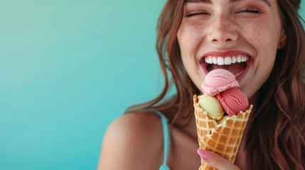 Foto auf Alu-Dibond A woman wearing a big smile as she enjoys a waffle cone filled with colorful ice cream on a mint blue background, closeup. Copy space. © Mosaic Media