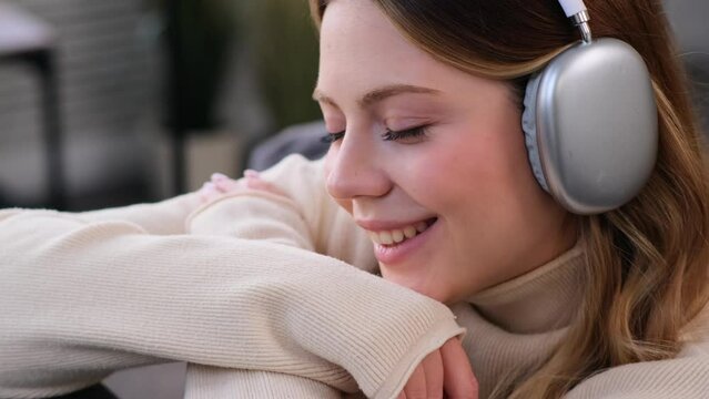 Close up portrait of a pleased and friendly Caucasian young woman listening music in headphones at home. Enjoying leisure time and retirement.