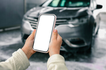 Hands with a blank phone screen on the background of a car wash