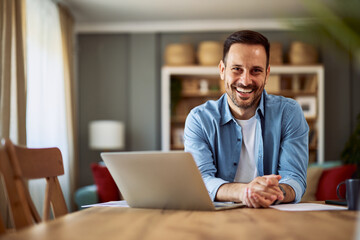 Portrait of a cheerful adult man holding his hands on a desk in front of a laptop for work.