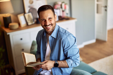 Portrait of a smiling young adult man holding a book from his home library.