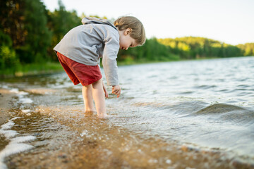 Cute little boy playing by a lake or river on hot summer day. Adorable child having fun outdoors...