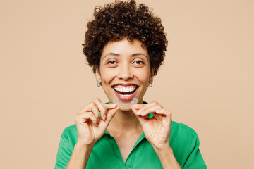 Young fun woman of African American ethnicity wear green shirt casual clothes hold orthodontic invisible aligner isolated on plain pastel beige background studio. Lifestyle, dental healthcare concept.