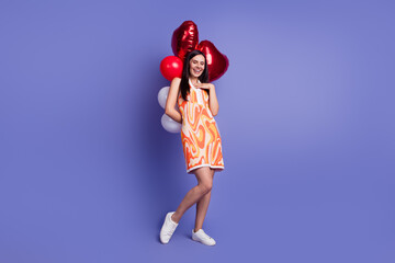 Full size photo of pretty young woman laugh hold balloons empty space wear dress isolated on violet color background