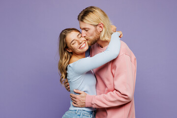 Side view young smiling lovely couple two friends family man woman wear pink blue casual clothes together hug cuddle embrace kissing isolated on pastel plain light purple background studio portrait.