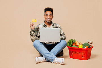 Full body young man wears grey shirt sit near red basket bag food products use laptop pc computer...