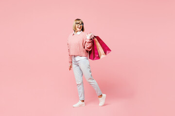 Full body elderly happy fun young woman wear casual clothes hold in hand paper package bags after shopping look aside isolated on plain light pastel pink background. Black Friday sale buy day concept. - obrazy, fototapety, plakaty