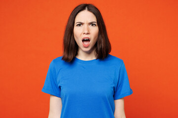 Young sad shocked astonished mad furious woman she wears blue t-shirt casual clothes looking camera with opened mouth isolated on plain red orange wall background studio portrait. Lifestyle concept. - obrazy, fototapety, plakaty