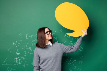 Young smart teacher woman wear grey casual shirt glasses empty blank Say cloud, speech bubble for content isolated on green wall chalk blackboard background. Education in high school college concept.