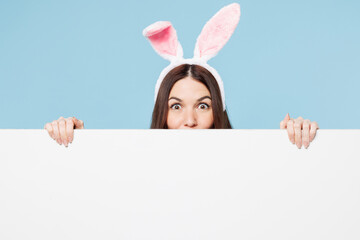 Close up shocked young woman wear pink casual clothes rabbit bunny ears hold big with white empty...