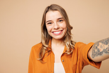 Close up young smiling happy woman she wear orange shirt casual clothes doing selfie shot pov on mobile cell phone isolated on plain pastel light beige background studio portrait. Lifestyle concept.