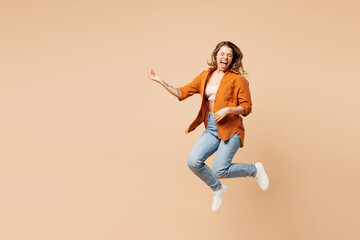Fototapeta na wymiar Full body expressive overjoyed cool singer young woman she wear orange shirt casual clothes jump high play air guitar isolated on plain pastel light beige background studio portrait Lifestyle concept