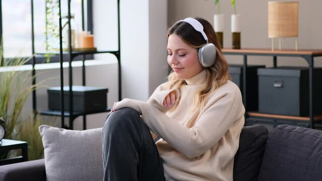 Peaceful Caucasian young woman resting on sofa at home during weekend leisure time and listening music in headphones. Relaxation and enjoyment concept.
