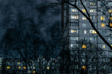 A residential building with the lights on in the windows on a cloudy evening