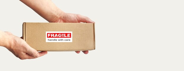 One rectangular cardboard box in hands for fragile items packing on a plain light background. An...