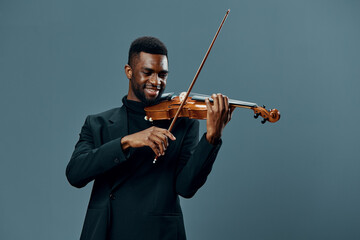 Talented young African American man in black suit performing on violin against gray background