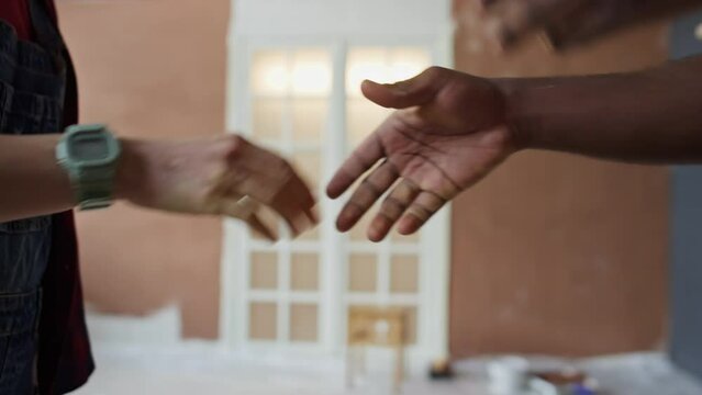Side cropped footage of hands of diverse partners shaking hands while making agreement about room renovation