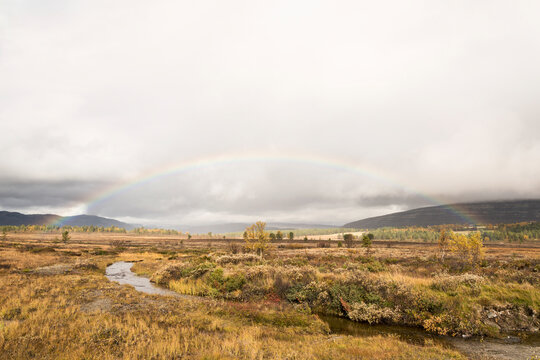View of Rainbow over valley with small brook in autumn, Rondane, Innlandet, Norway.