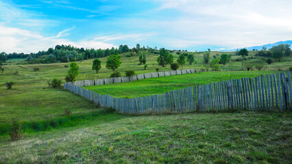 A wooden fence built on a hill. The meadows on the hill are used for farming or for orchards. Rural...