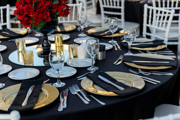 Romantic garden wedding reception with round tables, gold accents, and red rose centerpieces