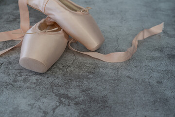 Two pink ballet slippers are on a grey surface - obrazy, fototapety, plakaty