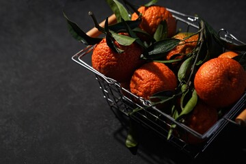 Fresh ripe mandarines with green leaves in the metal shopping basket on a black background,...