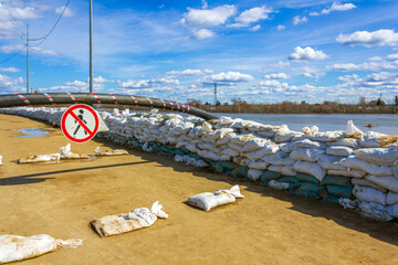 The stop sign stands near the wall of white sandbags, which has been erected as a barricade for flood protection, with a flooded embankment in the background.